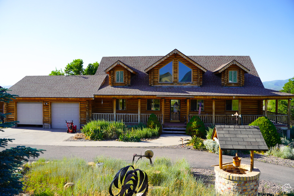 Log home featuring a porch, a garage, concrete driveway, log exterior, and roof with shingles