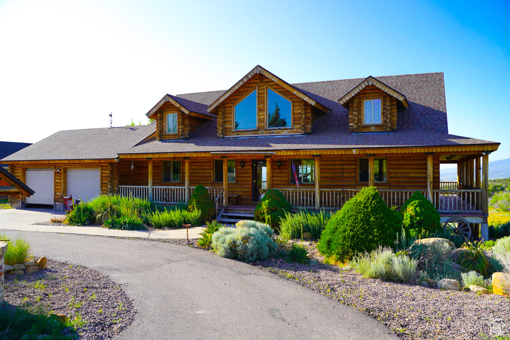 Log home featuring log exterior, a garage, covered porch, and driveway