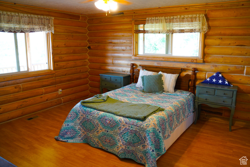 Bedroom featuring wood finished floors, log walls, and multiple windows