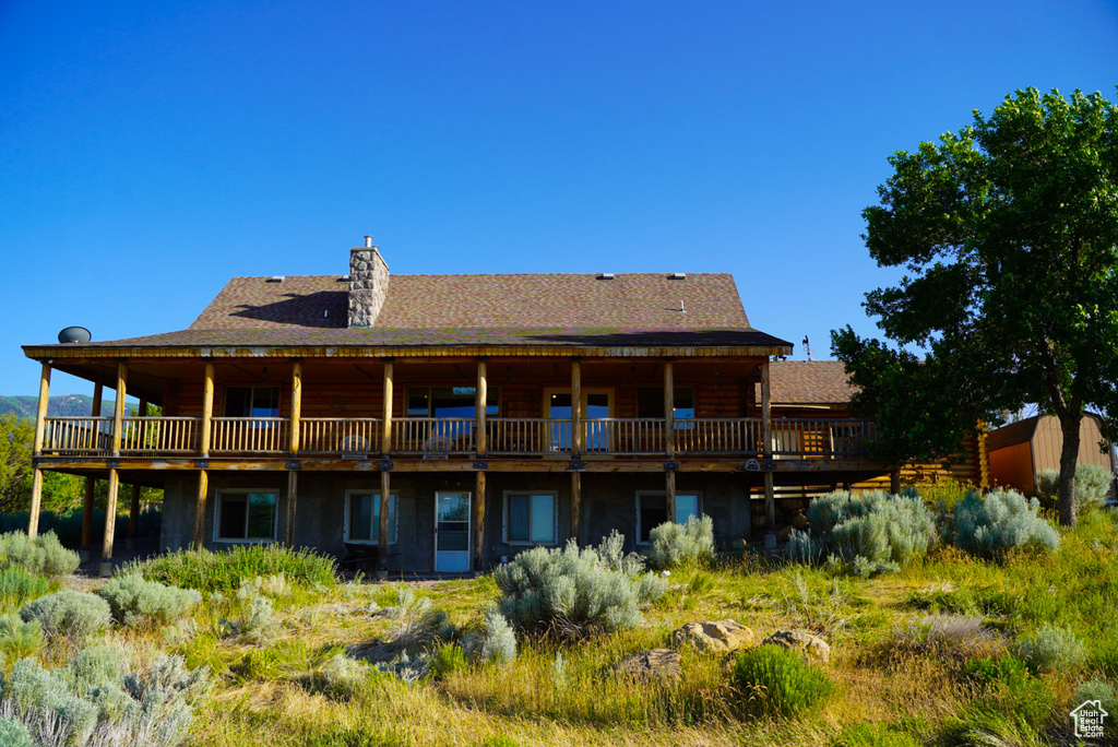 Back of property featuring log siding, a chimney, a wooden deck, and a shingled roof