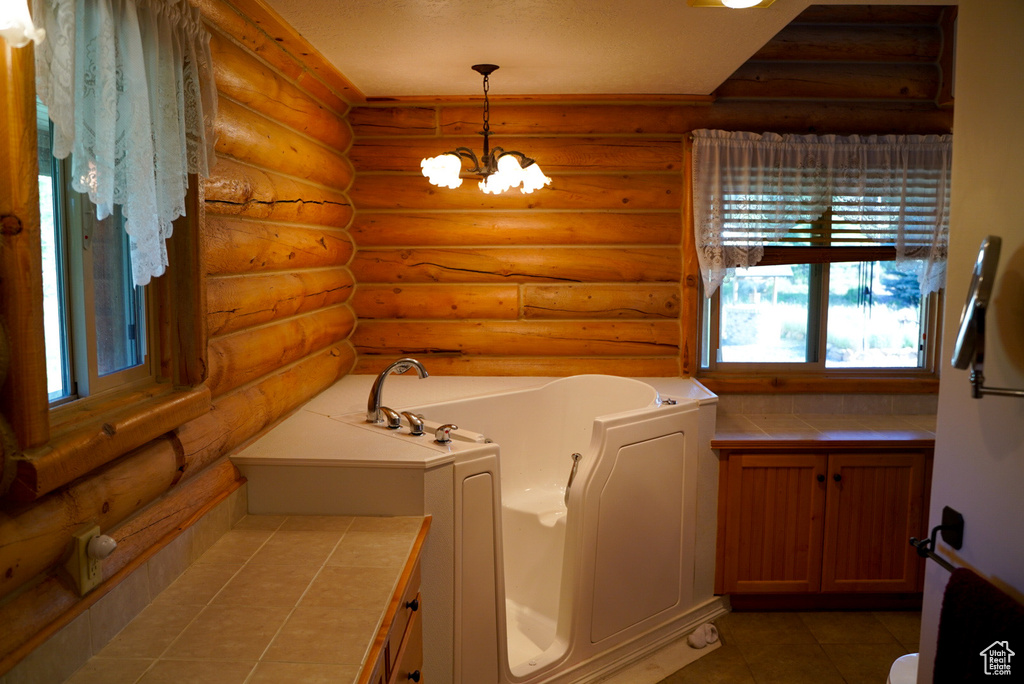 Bathroom with a bath, rustic walls, a chandelier, and tile patterned flooring