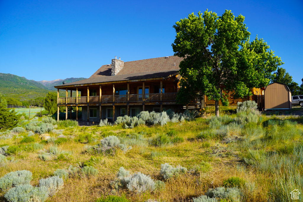 Rear view of property with a storage unit, a deck with mountain view, a chimney, and roof with shingles