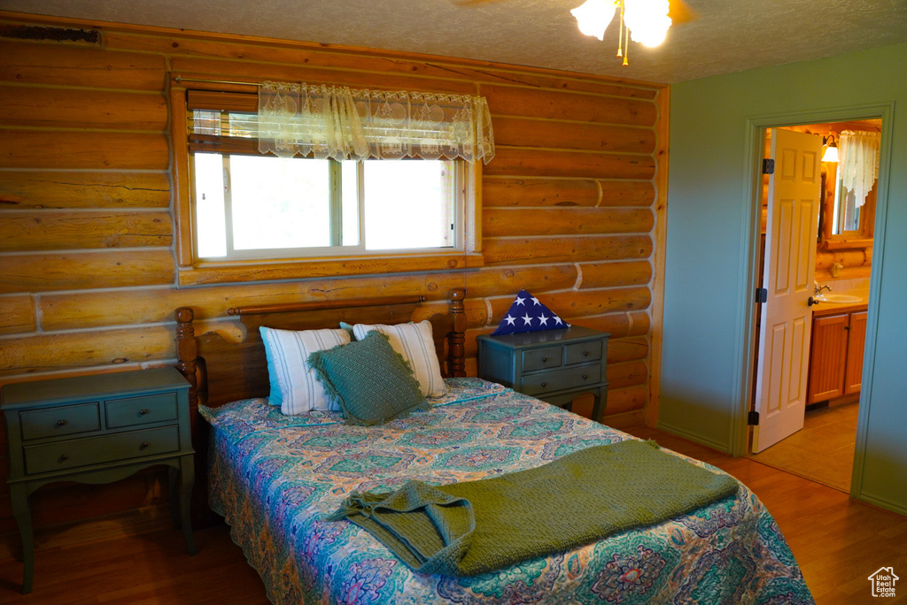 Bedroom with log walls, light wood finished floors, a textured ceiling, and ensuite bathroom
