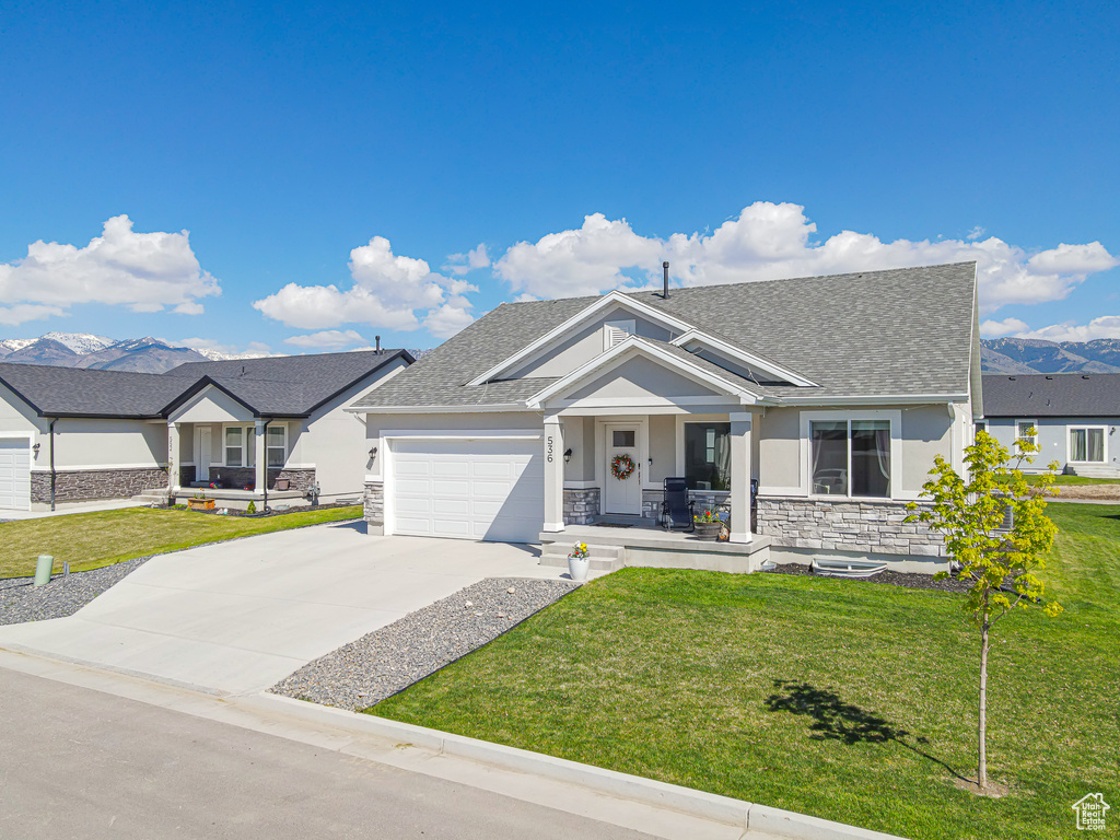 View of front of property featuring a porch, a shingled roof, stone siding, and a front yard