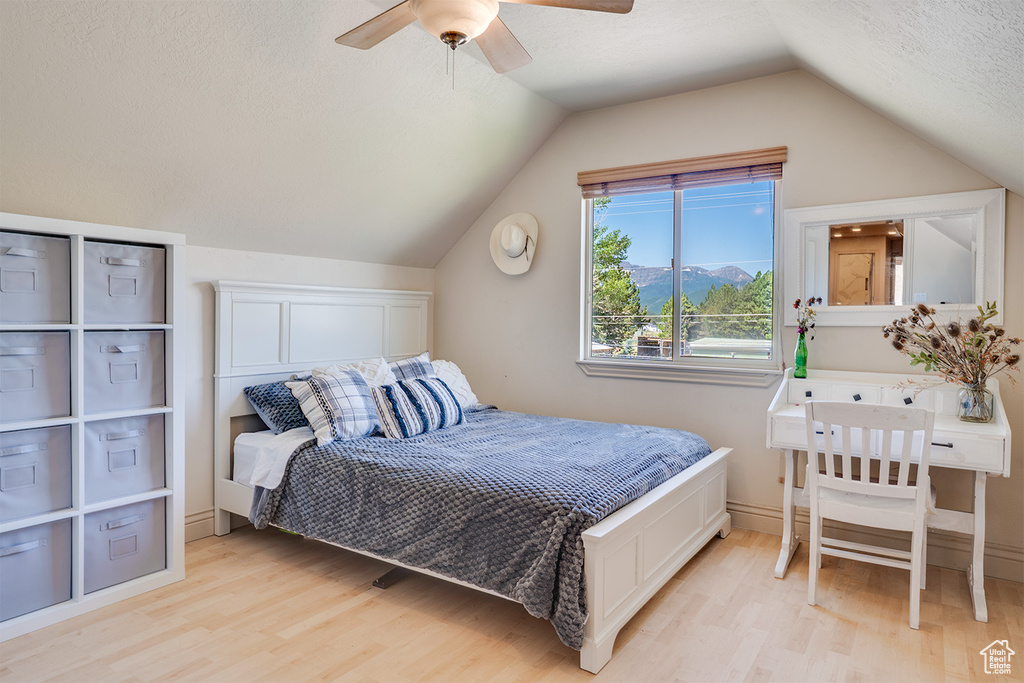 Bedroom with light wood-style flooring, lofted ceiling, a ceiling fan, and a textured ceiling