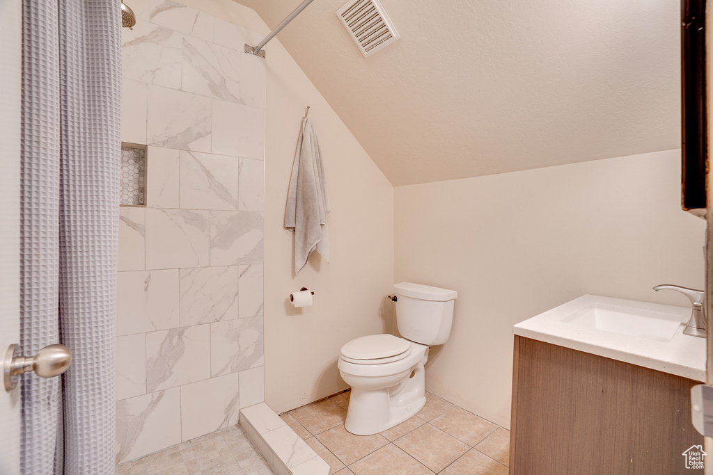 Bathroom with lofted ceiling, a tile shower, vanity, and tile patterned floors