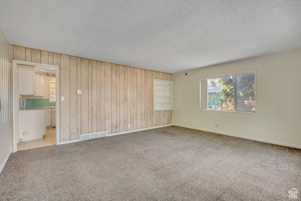 Empty room with wooden walls, a textured ceiling, and light colored carpet