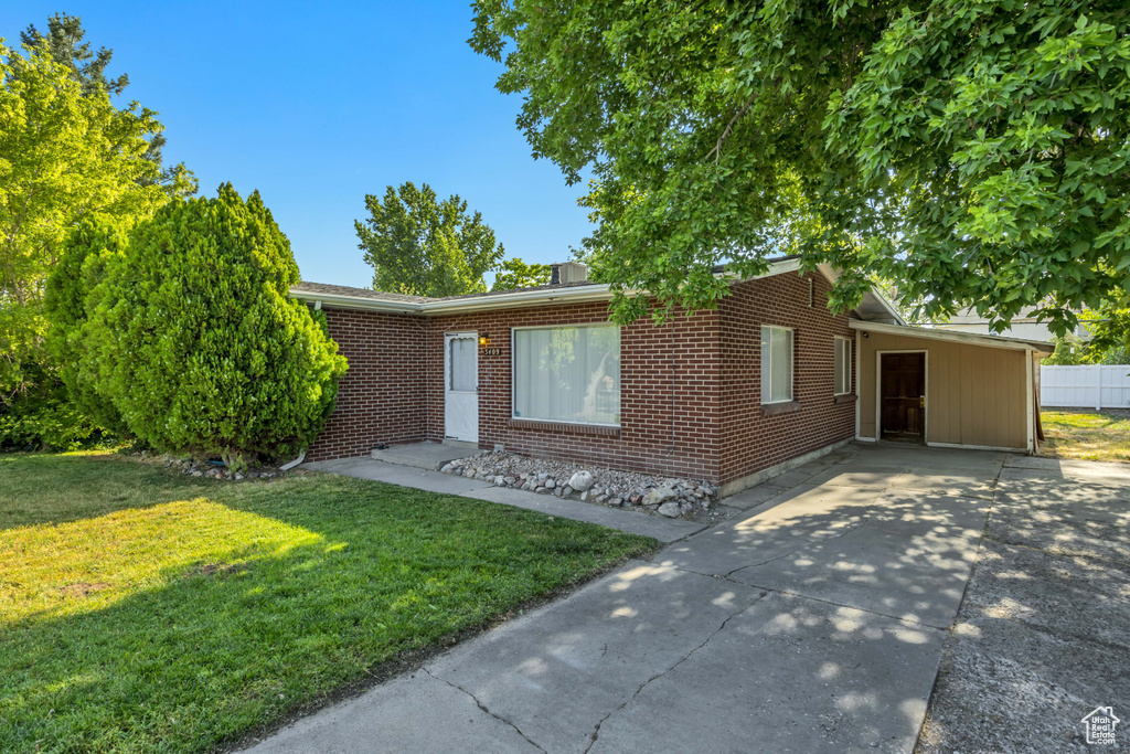 Ranch-style home featuring a front lawn, driveway, brick siding, and an attached carport