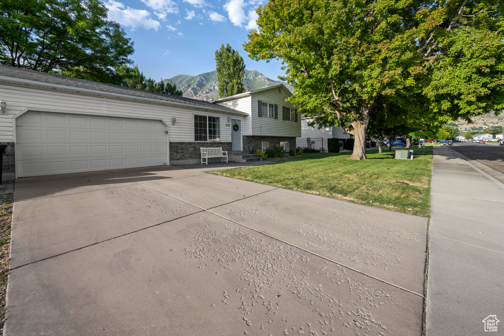 Tri-level home with a mountain view, concrete driveway, a front yard, and an attached garage