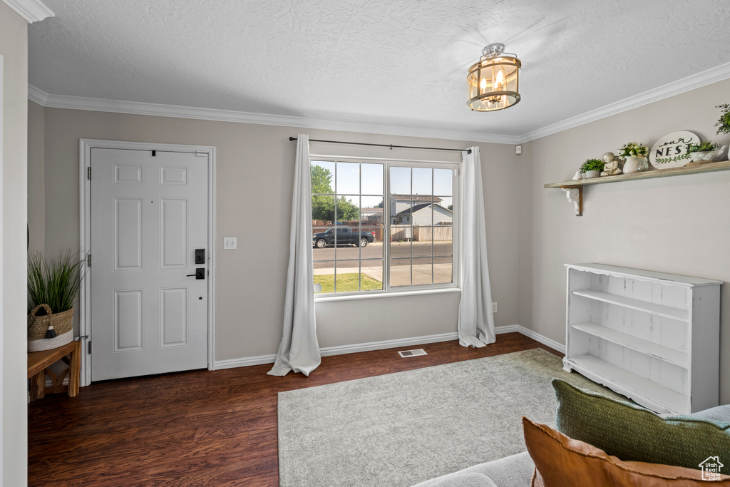 Foyer entrance with wood finished floors, ornamental molding, a textured ceiling, and a chandelier