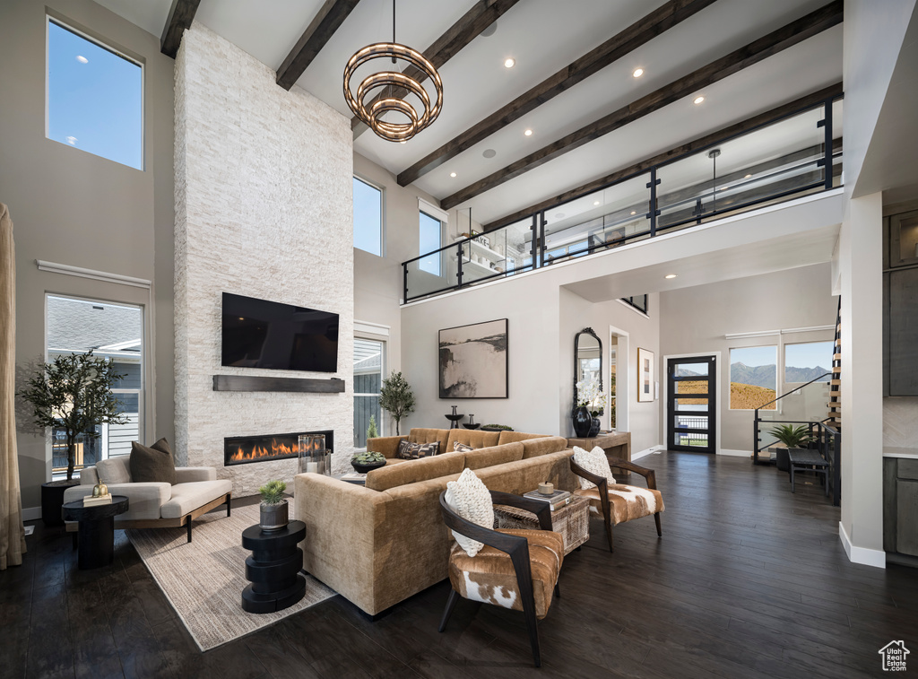 Living area featuring a towering ceiling, a stone fireplace, beam ceiling, healthy amount of natural light, and a chandelier