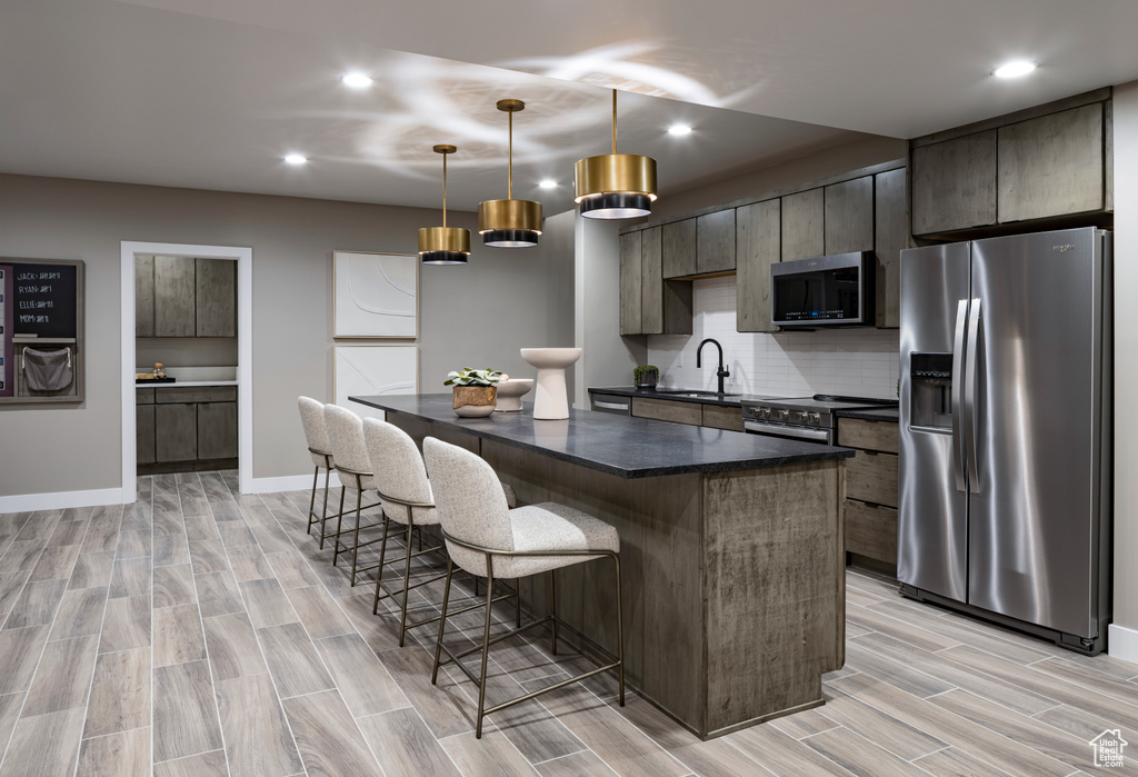 Kitchen featuring appliances with stainless steel finishes, a kitchen bar, a kitchen island, recessed lighting, and light wood-style flooring