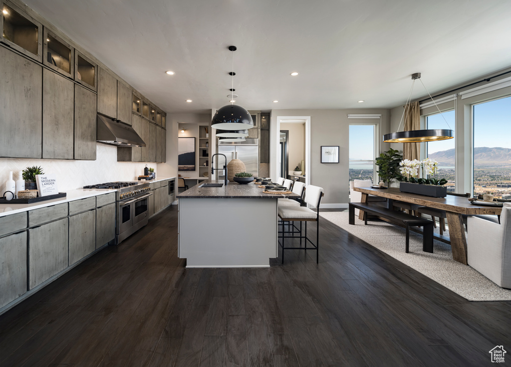 Kitchen with high end appliances, under cabinet range hood, recessed lighting, dark wood finished floors, and a breakfast bar area