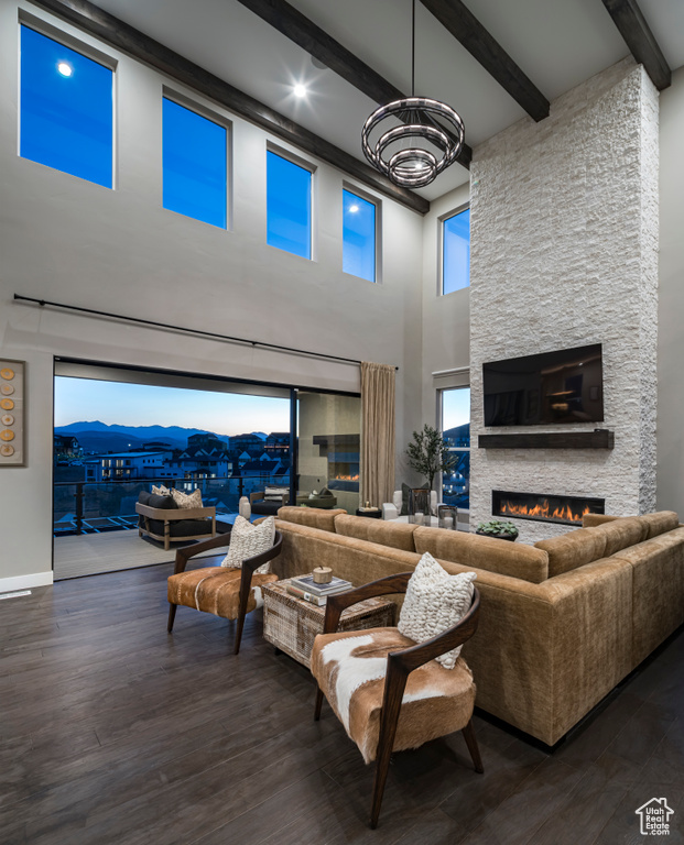 Living room featuring beamed ceiling, a chandelier, a towering ceiling, wood finished floors, and a fireplace