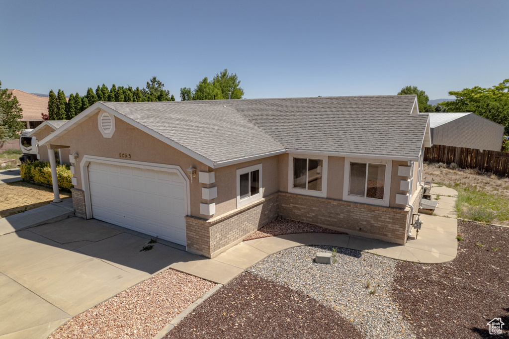 Single story home with brick siding, a garage, roof with shingles, concrete driveway, and stucco siding