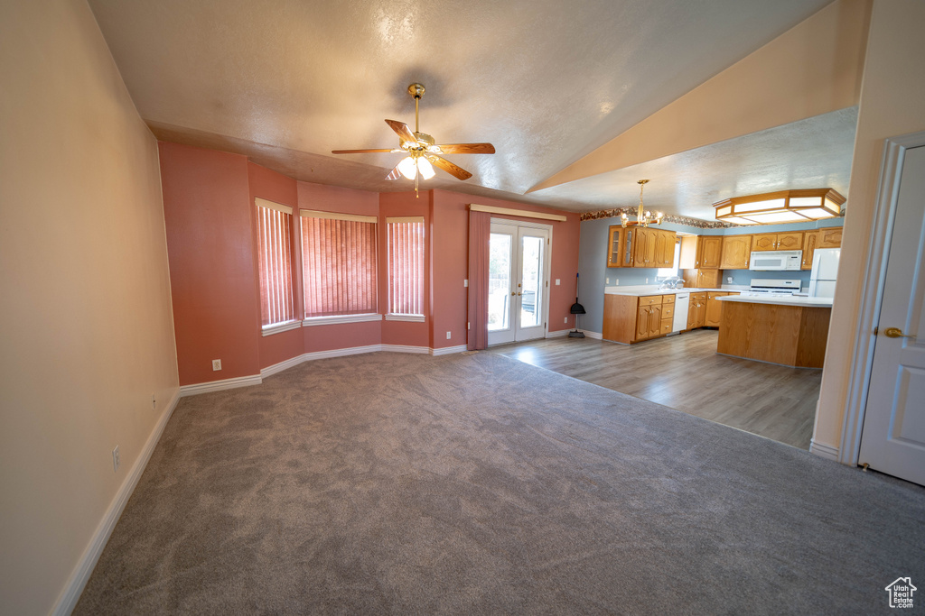 Unfurnished living room featuring light carpet, ceiling fan, a chandelier, and vaulted ceiling