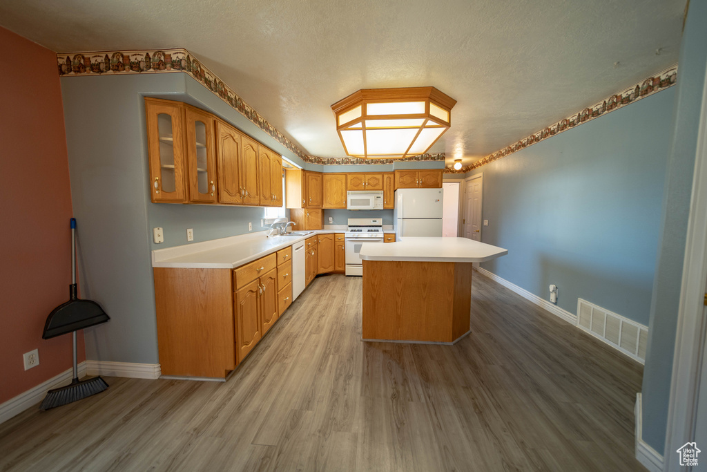 Kitchen with white appliances, light wood finished floors, light countertops, glass insert cabinets, and a textured ceiling