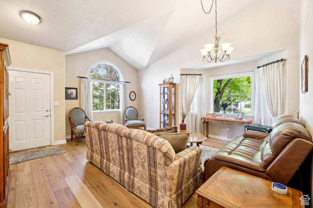 Living room with light wood-type flooring, healthy amount of natural light, a chandelier, and vaulted ceiling