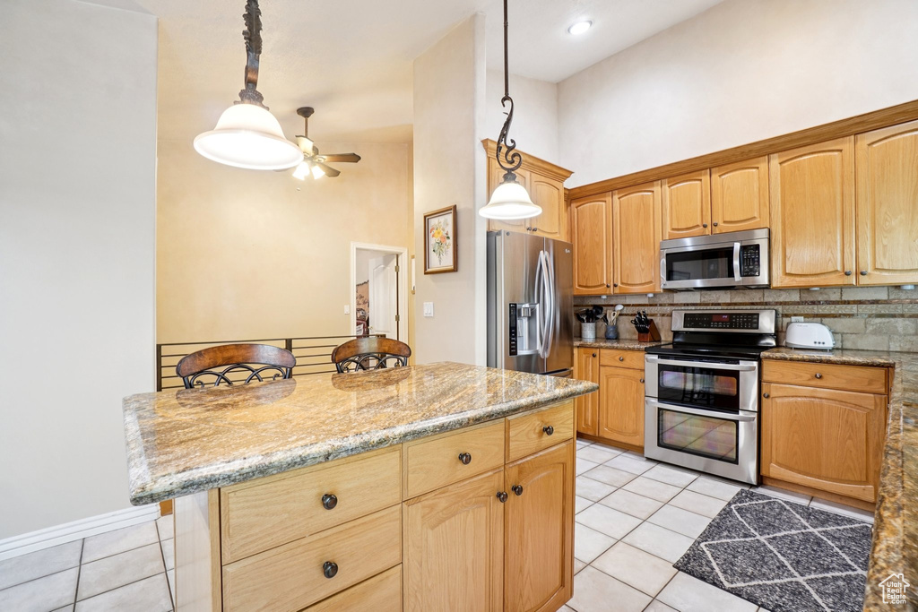Kitchen with appliances with stainless steel finishes, light tile patterned flooring, decorative backsplash, ceiling fan, and pendant lighting