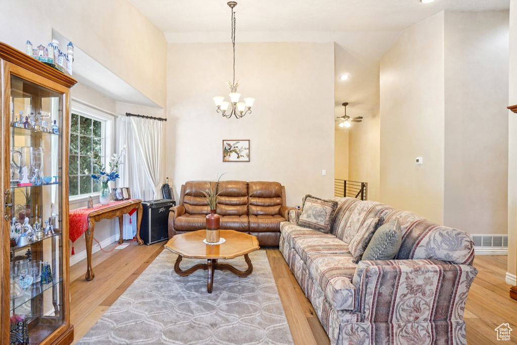 Living room with a chandelier, light wood-style flooring, lofted ceiling, and ceiling fan