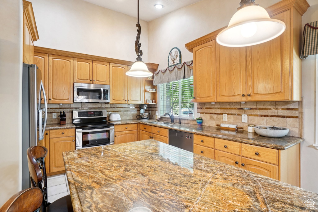 Kitchen featuring appliances with stainless steel finishes, a high ceiling, decorative backsplash, pendant lighting, and dark stone countertops
