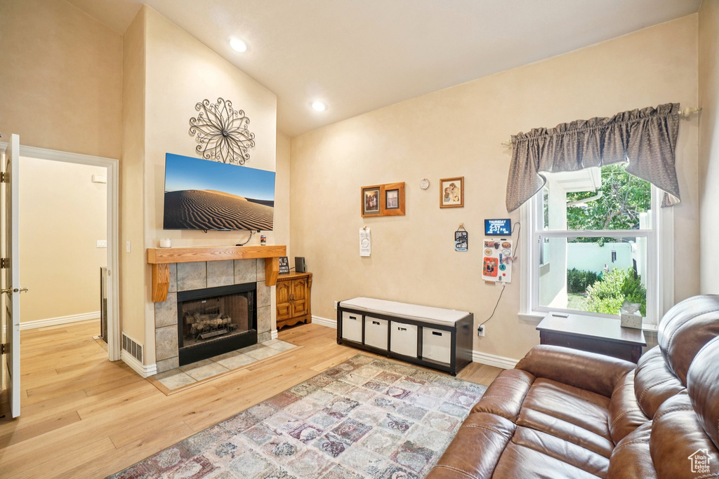 Living room with wood finished floors, a tiled fireplace, and recessed lighting