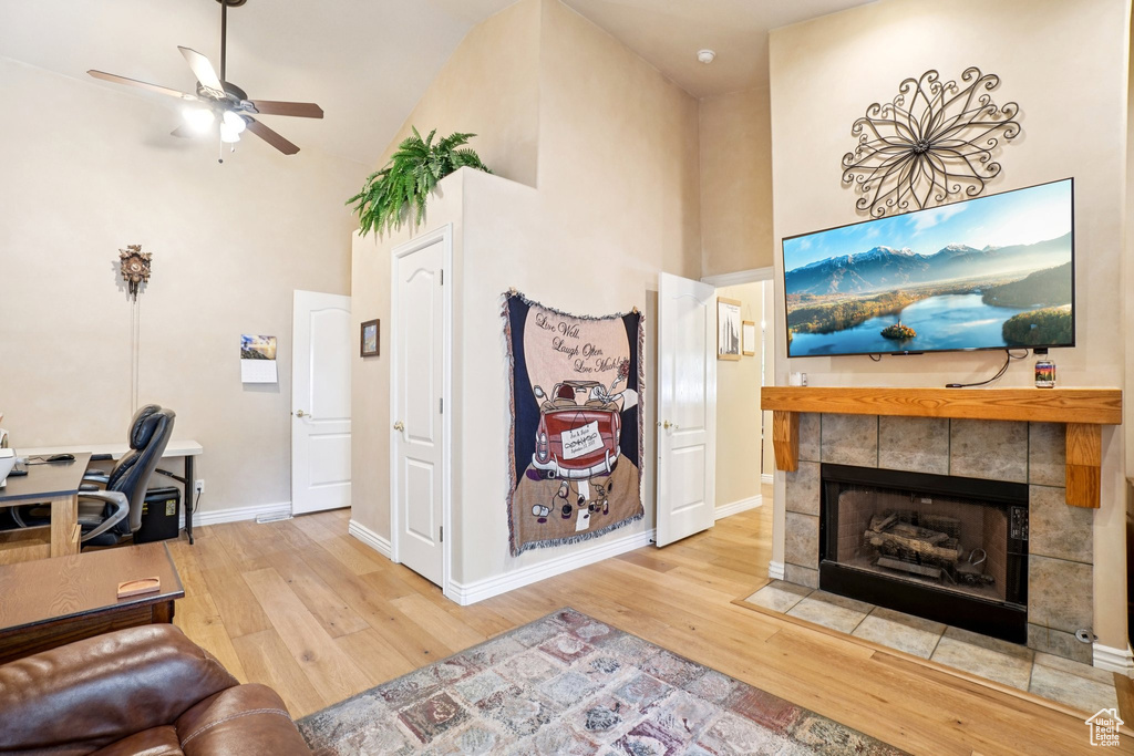 Living area featuring a towering ceiling, wood finished floors, ceiling fan, a fireplace, and a desk