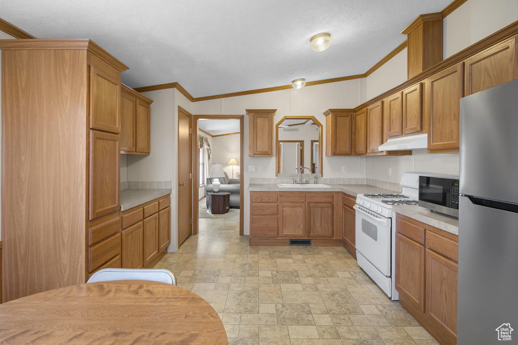 Kitchen with appliances with stainless steel finishes, under cabinet range hood, light countertops, brown cabinets, and ornamental molding