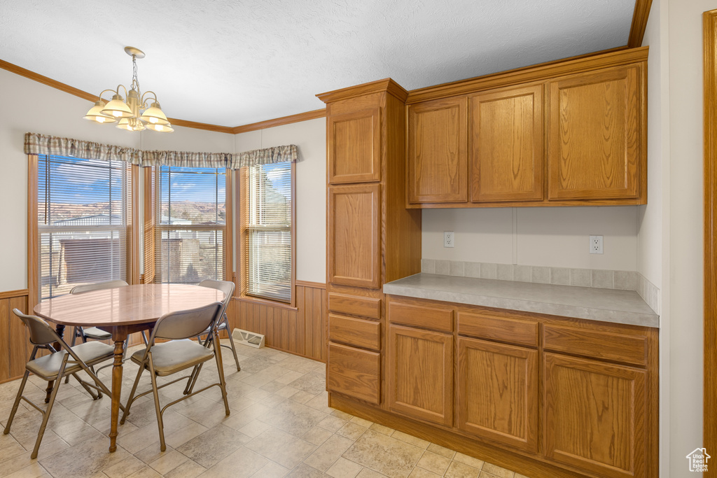 Dining space with a wainscoted wall, a chandelier, ornamental molding, light stone finish floors, and wood walls