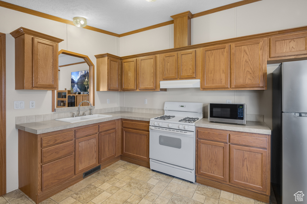 Kitchen featuring appliances with stainless steel finishes, under cabinet range hood, light countertops, brown cabinets, and ornamental molding