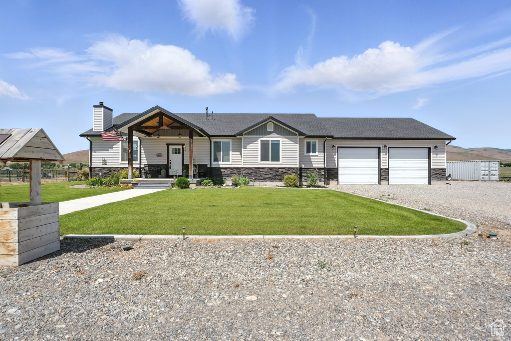 View of front of house with gravel driveway, stone siding, an attached garage, a front yard, and a chimney