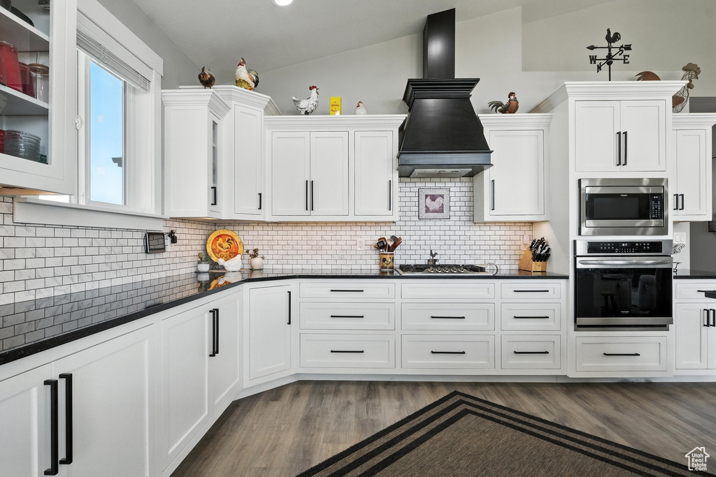 Kitchen featuring stainless steel appliances, premium range hood, dark countertops, and white cabinetry