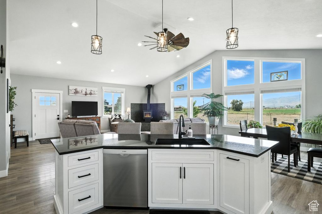 Kitchen featuring stainless steel dishwasher, dark countertops, ceiling fan, a wood stove, and open floor plan
