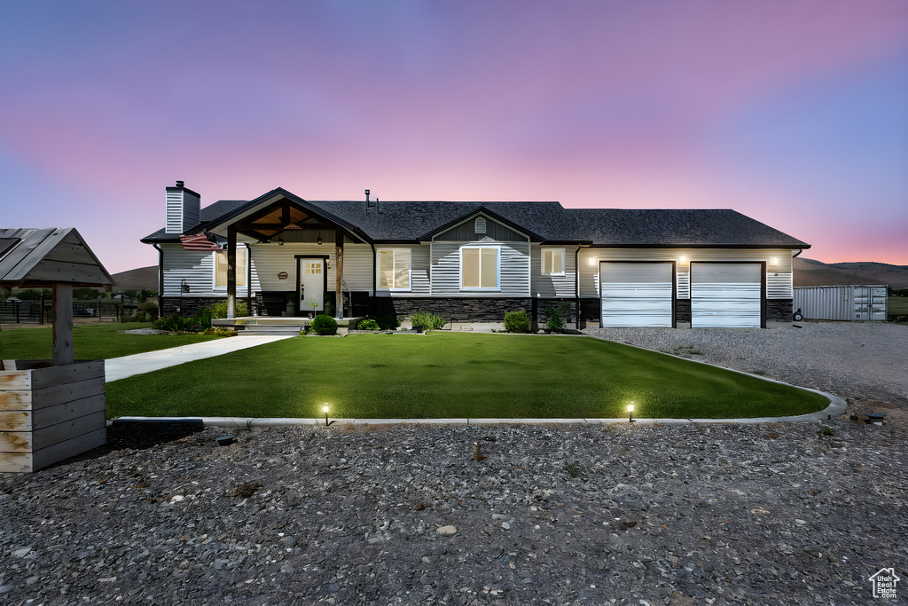 View of front facade with gravel driveway, a garage, a chimney, a front lawn, and stone siding