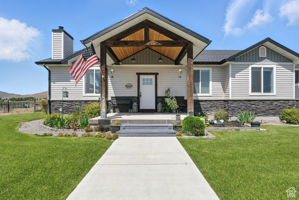 View of front of property featuring stone siding, a front yard, covered porch, a chimney, and board and batten siding