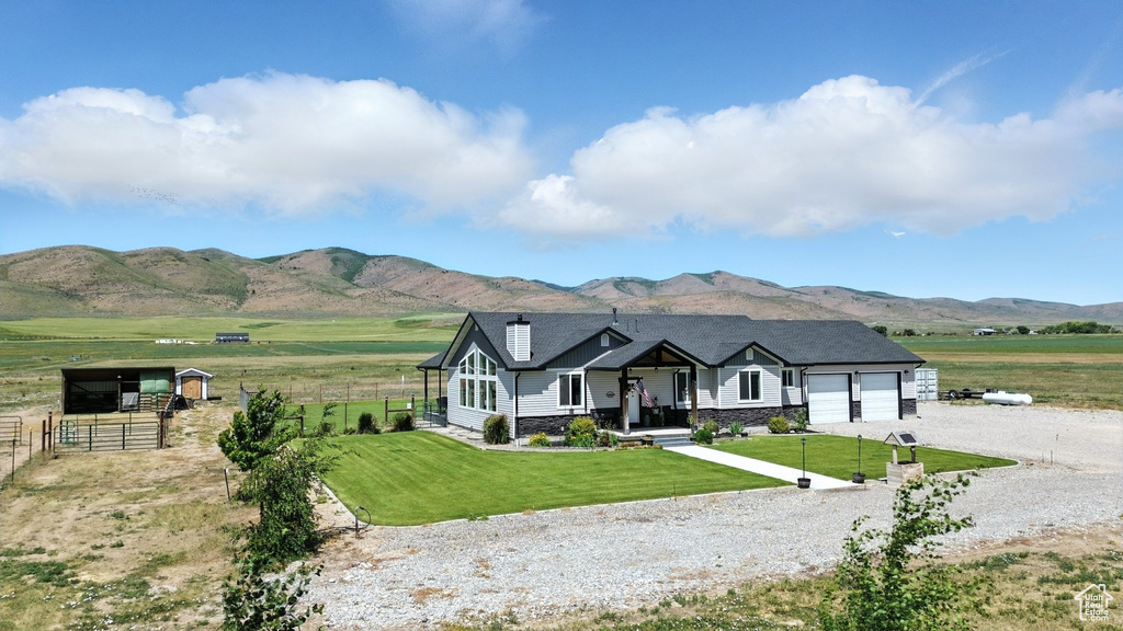 View of front of property featuring driveway, an attached garage, a mountain view, stone siding, and a rural view