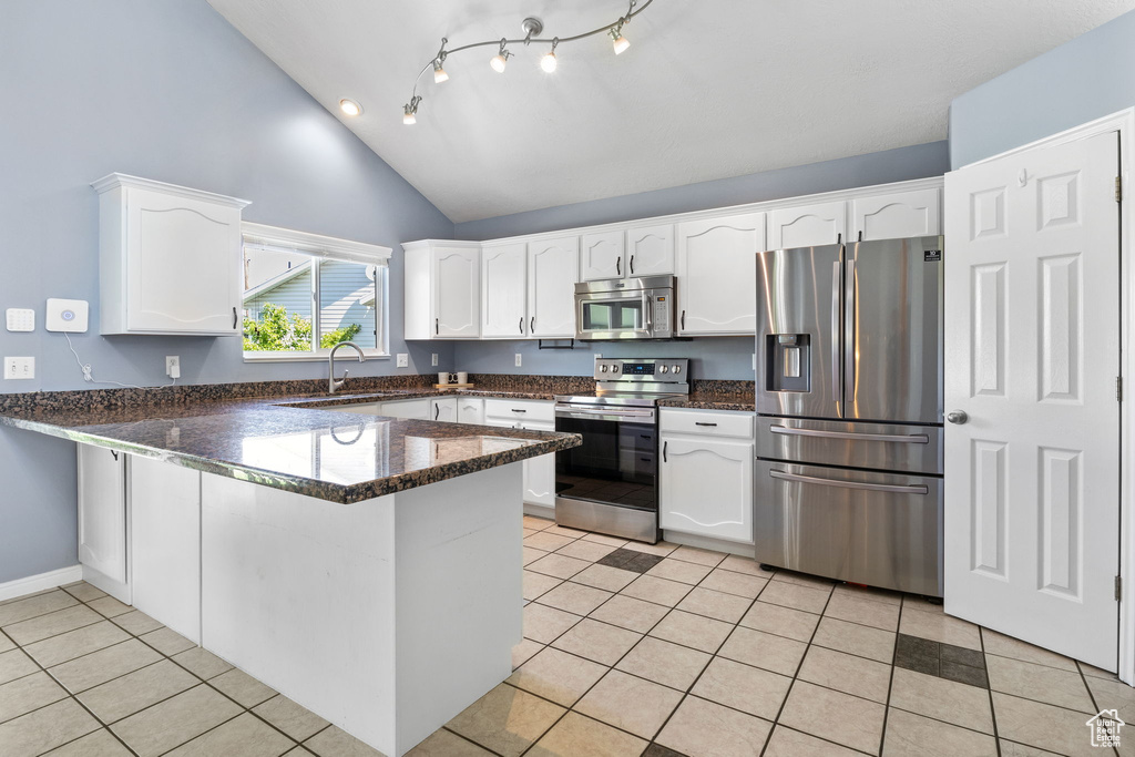 Kitchen featuring appliances with stainless steel finishes, a peninsula, white cabinetry, light tile patterned floors, and high vaulted ceiling