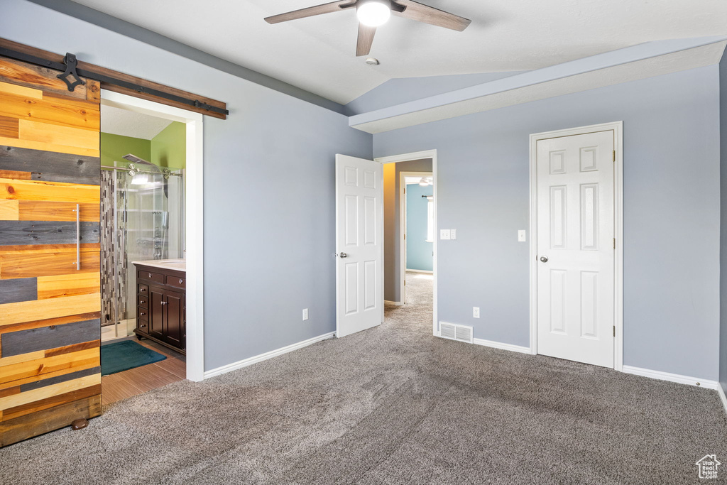 Unfurnished bedroom with carpet flooring, a barn door, lofted ceiling, connected bathroom, and ceiling fan