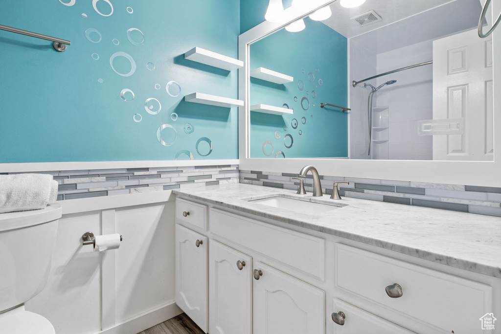 Full bathroom featuring vanity, backsplash, a shower, and wood finished floors