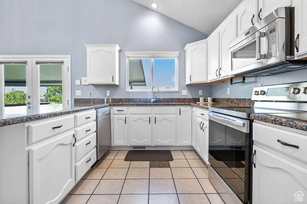 Kitchen featuring stainless steel appliances, white cabinets, light tile patterned floors, high vaulted ceiling, and french doors