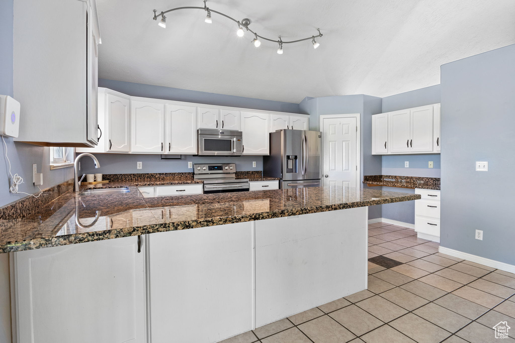 Kitchen featuring stainless steel appliances, a peninsula, light tile patterned floors, white cabinets, and dark stone countertops