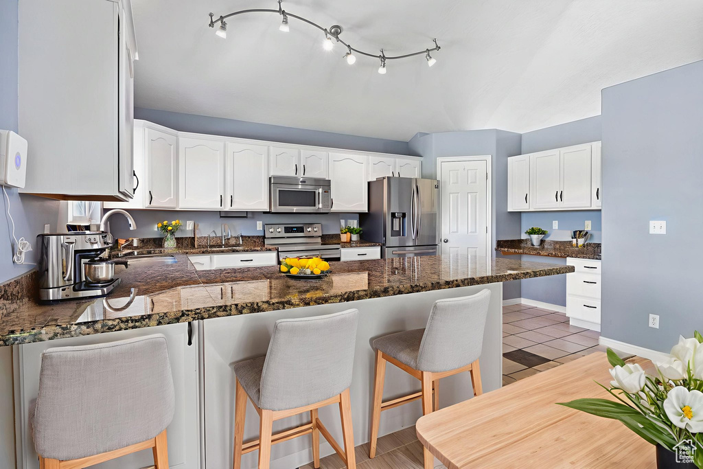Kitchen with appliances with stainless steel finishes, a peninsula, white cabinetry, a breakfast bar, and dark stone counters