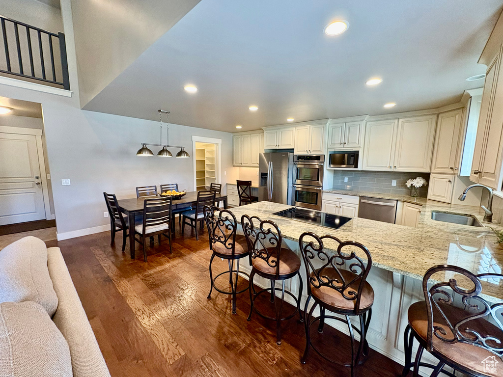 Kitchen with appliances with stainless steel finishes, a peninsula, light stone countertops, a breakfast bar area, and dark wood-style flooring