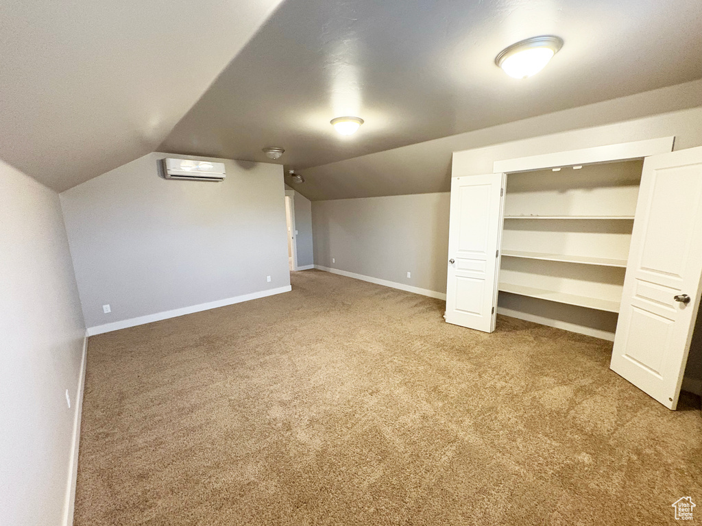Bonus room with a wall mounted air conditioner, carpet flooring, and lofted ceiling