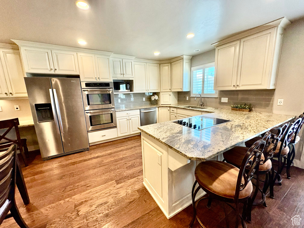 Kitchen featuring stainless steel appliances, a peninsula, light wood-style floors, a kitchen bar, and light stone counters