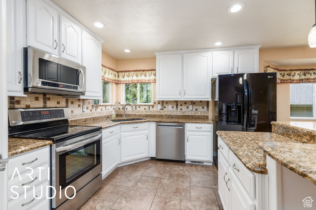 Kitchen featuring appliances with stainless steel finishes, decorative backsplash, white cabinetry, light stone countertops, and recessed lighting