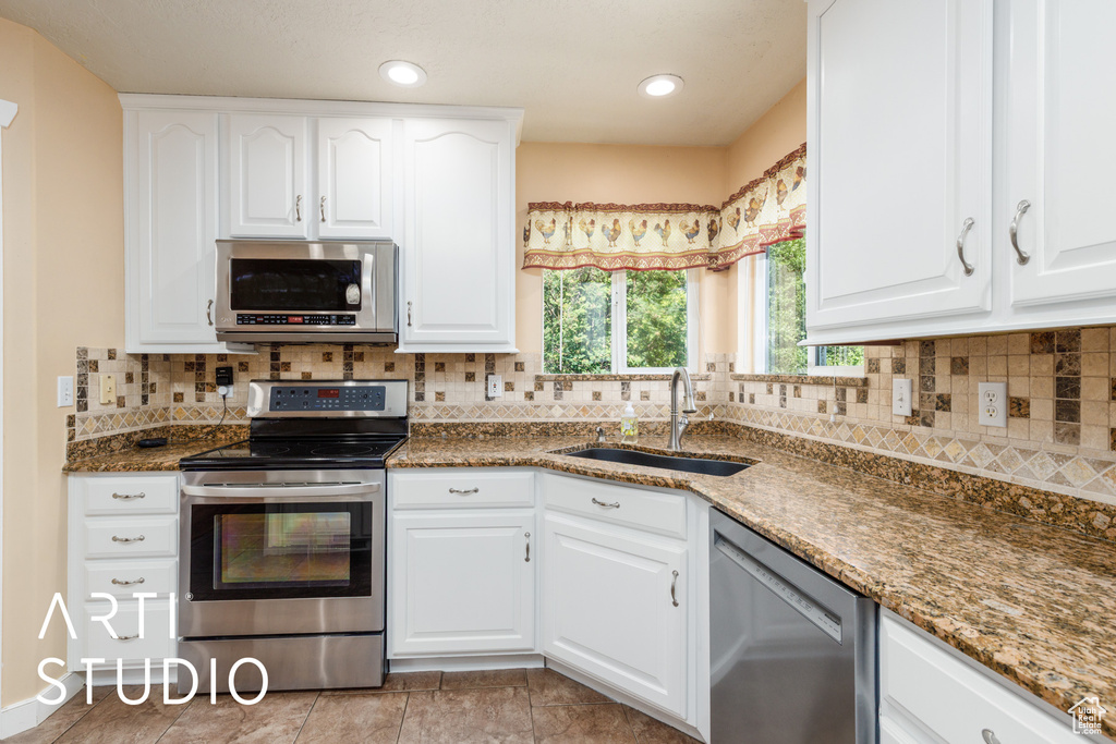 Kitchen with appliances with stainless steel finishes, dark stone countertops, white cabinets, decorative backsplash, and recessed lighting