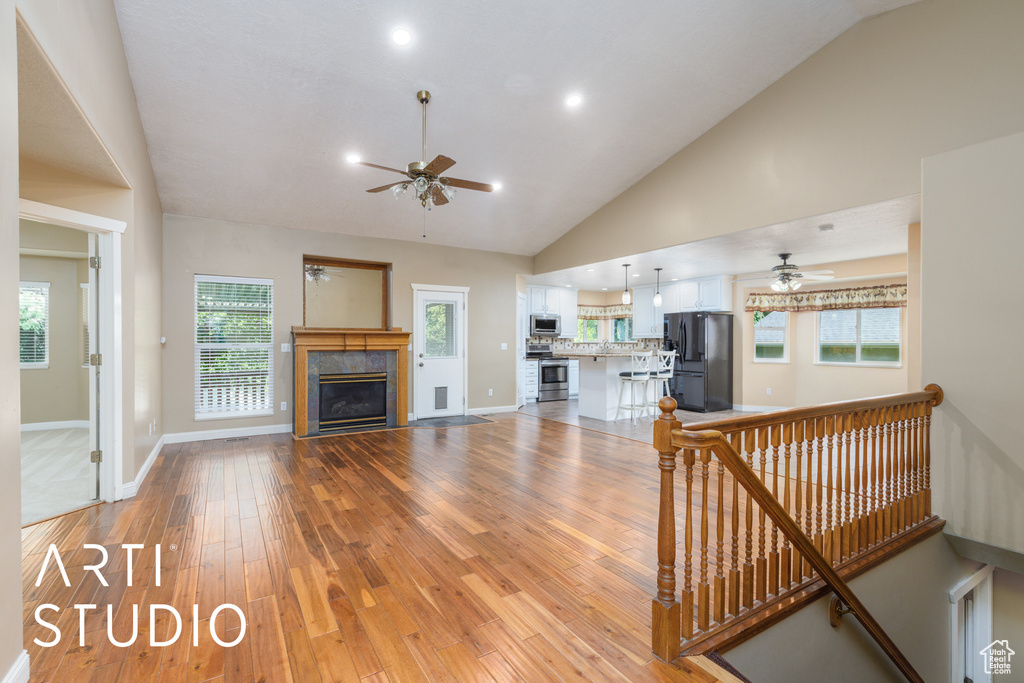 Living room featuring a ceiling fan, light wood-style flooring, vaulted ceiling, a glass covered fireplace, and recessed lighting