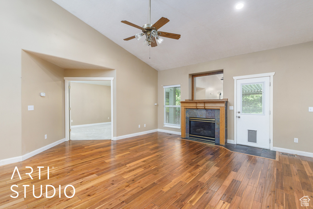 Unfurnished living room featuring ceiling fan, hardwood / wood-style floors, plenty of natural light, a tile fireplace, and high vaulted ceiling