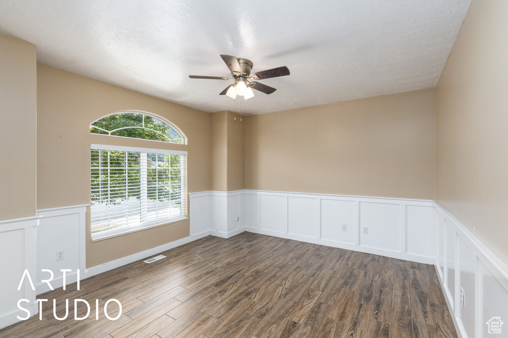 Spare room featuring dark wood finished floors, a ceiling fan, a wainscoted wall, a decorative wall, and a textured ceiling
